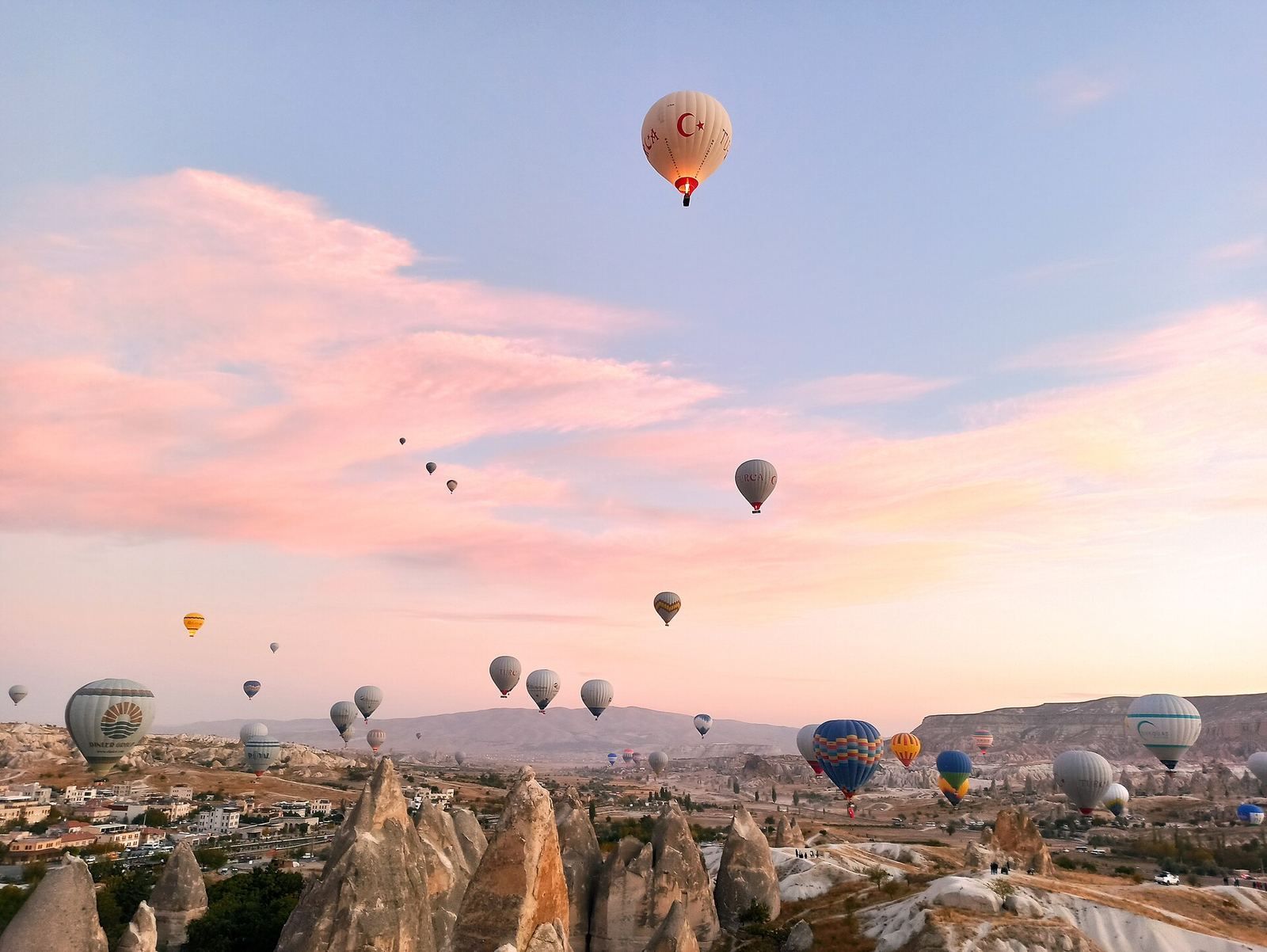 Dziesiątki balonów na różowym porannym niebie nad Göreme