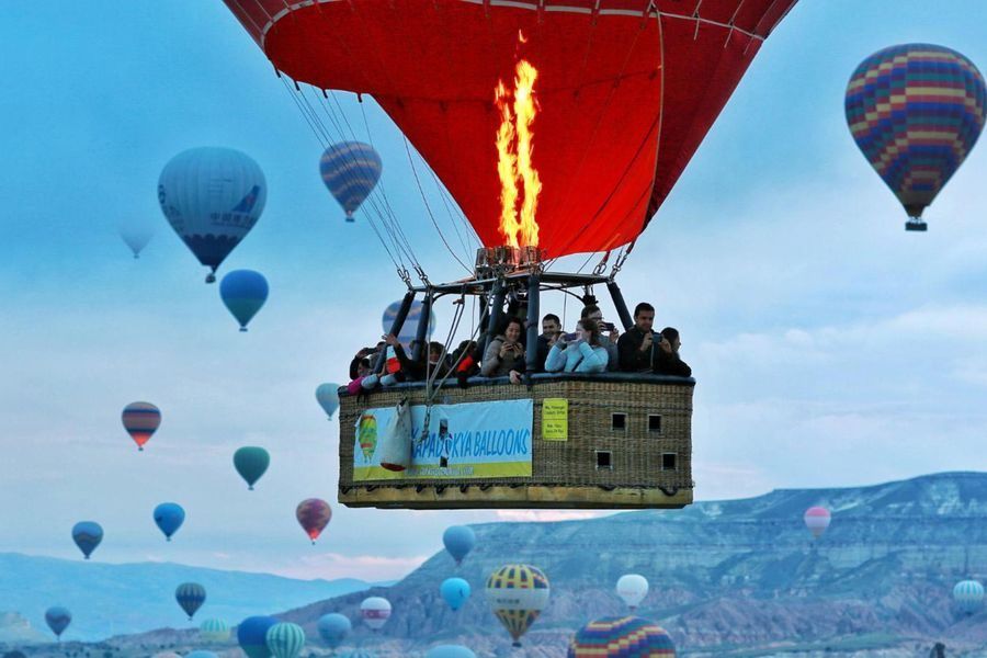 Pasażerowie w koszu balonu nad Kapadocją, nad nimi płomień palnika i inne balony
