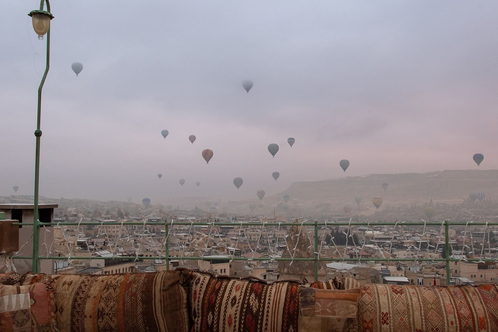 Taras z poduszkami nad Göreme o świcie, w tle balony nad Kapadocją